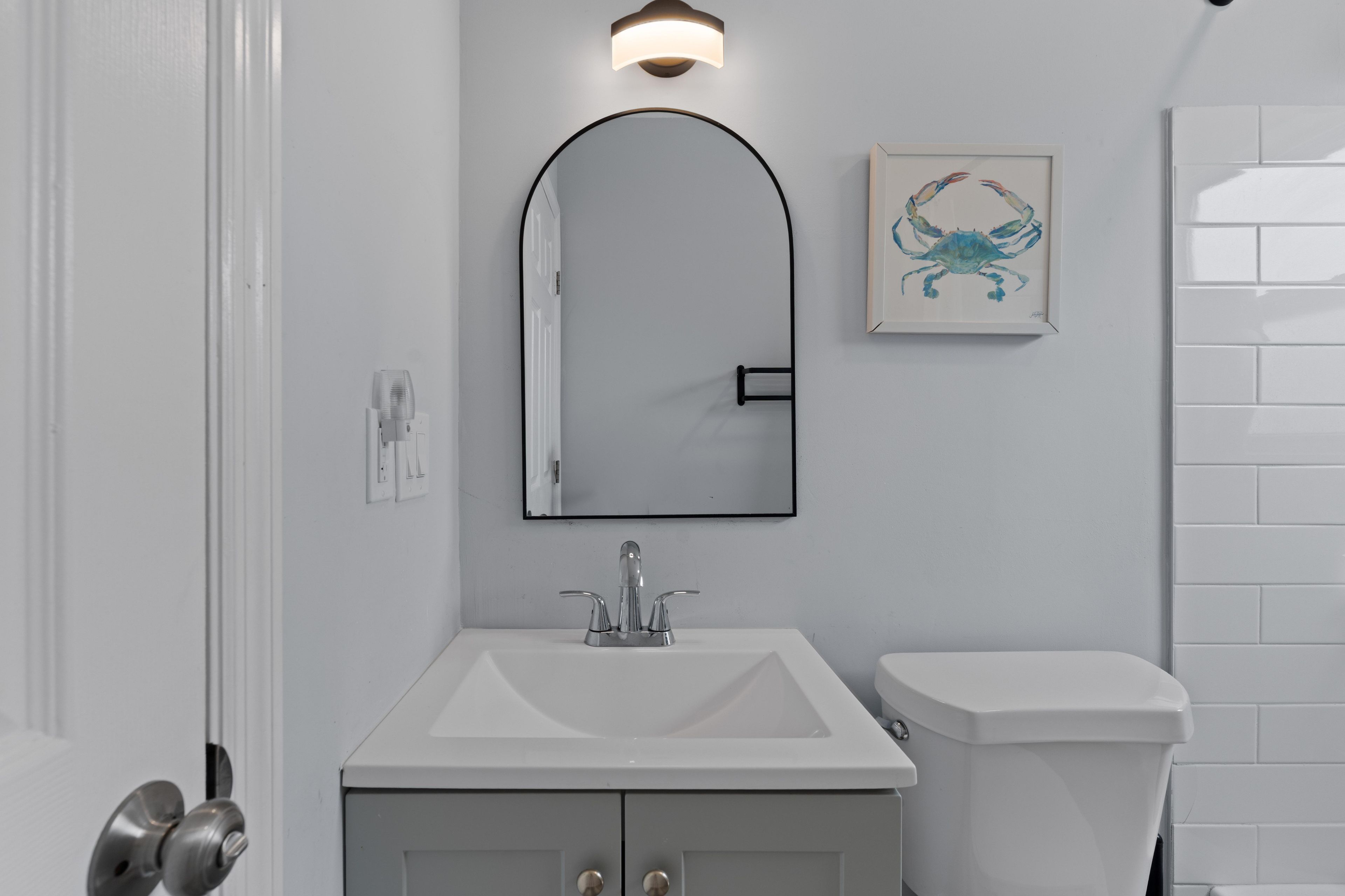 Ein Badezimmer mit weißem Waschbecken, Toilette, Spiegel mit schwarzem Rahmen und einer Wandleuchte.
