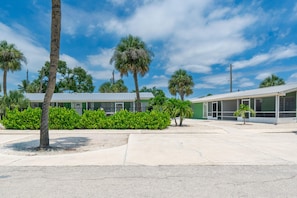 A building with a green facade, a parking lot, and palm trees.
