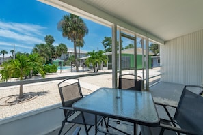 A covered outdoor area with a table and chairs, a view of a pool, and palm trees.