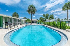 A swimming pool with a clear blue water, surrounded by a fence, and palm trees in the background.