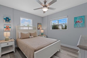 A bedroom with a bed, nightstands, a ceiling fan, and artwork on the walls.