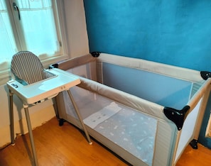 Ein Babyreisebett mit Tablett und hochaufliegendem Stuhl.