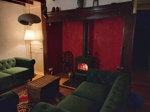 Ein gemütliches Wohnzimmer mit grün gepolsterten Möbeln, einer roten Akzentwand, einem Kaminofen und einer Hängelampe.