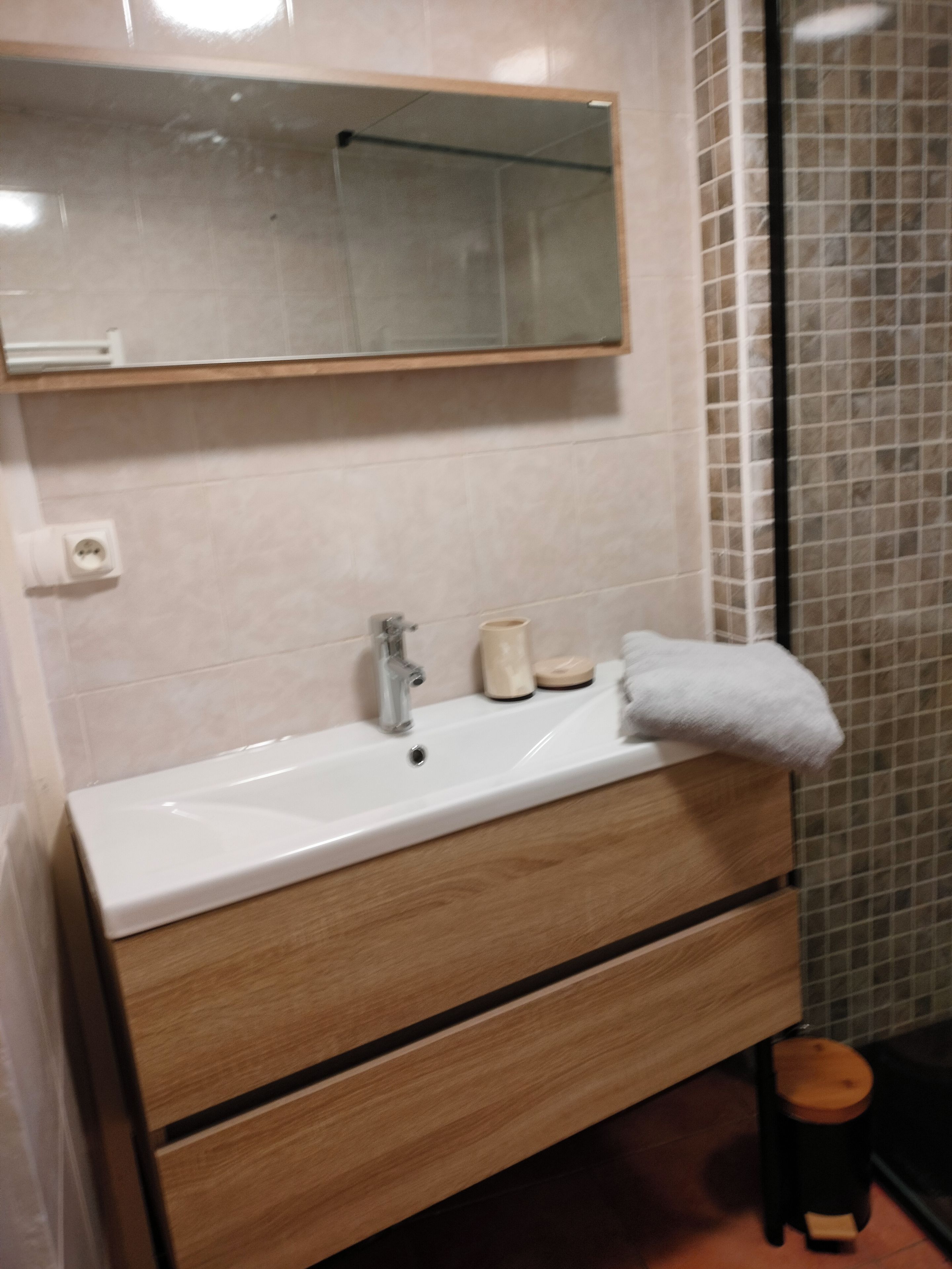A bathroom with a white sink, wooden vanity, a mirror, and a tiled shower area.