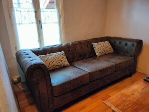 Eine braune Ledersofa mit zwei gemusterten Kissen, einem Holztisch und einem Fenster mit Vorhängen.
