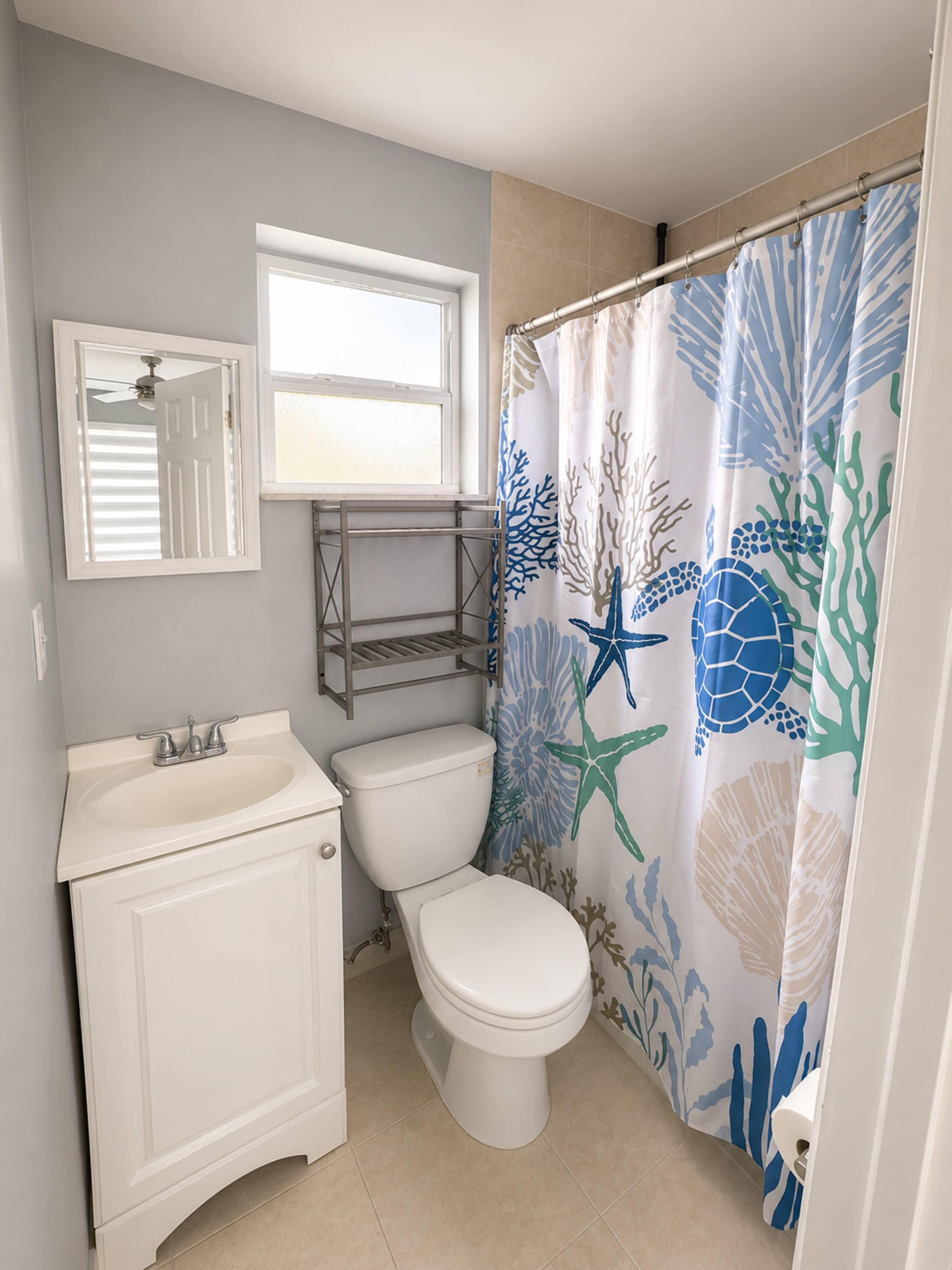 A bathroom with a toilet, sink, and shower curtain featuring marine life.