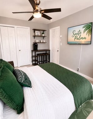A bedroom with a bed, a ceiling fan, a coffee table, and a wall-mounted TV displaying 'Suite Palma'. - Suite Palma – Private Studio with Pool Access (Deerfield Beach)
