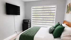 A bedroom with a bed, a ceiling fan, a TV, a window with blinds, and a small black appliance. - Suite Palma – Private Studio with Pool Access (Deerfield Beach)