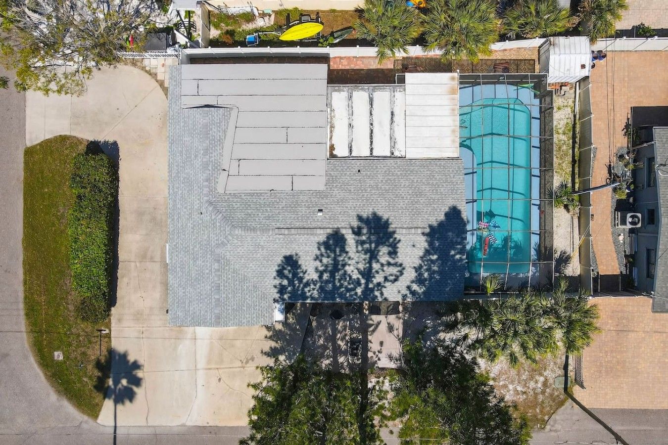 An aerial view of a building with a swimming pool, a covered patio area, and surrounding greenery.