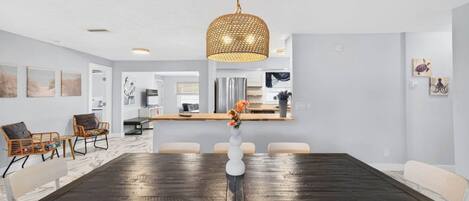 A dining area with a dark wooden table, white chairs, and a hanging light fixture.