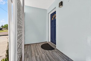 Varanda com porta azul escura, parede branca e chão de madeira.