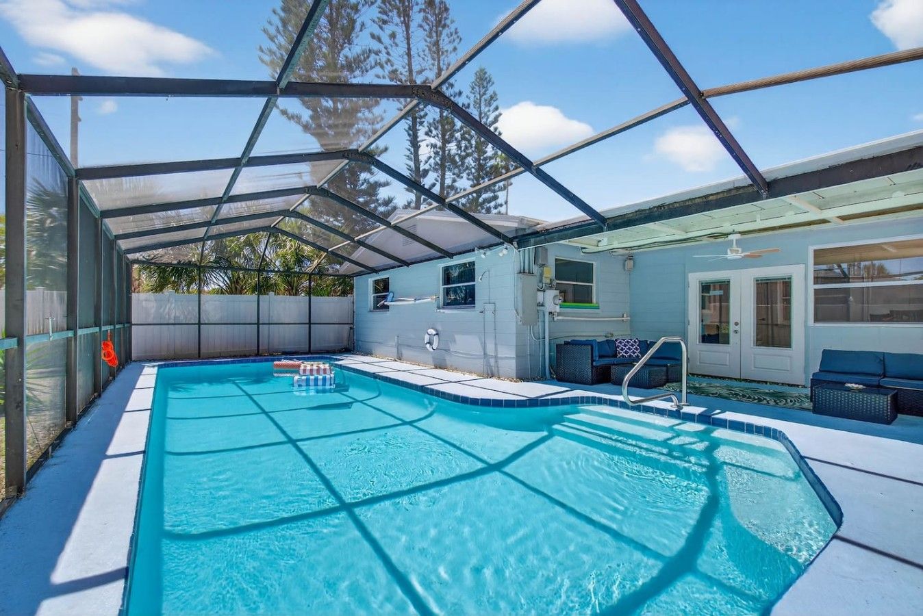 A covered swimming pool with a sunshade, a lounge area with seating, and a view of the surrounding trees.