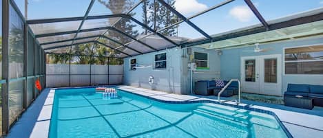 A covered swimming pool with a sunshade, a lounge area with seating, and a view of the surrounding trees.