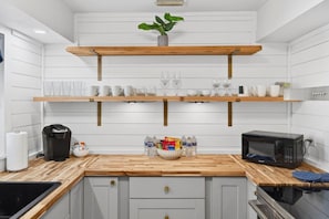 A kitchen with white cabinetry, wooden countertops, a coffee maker, a microwave, and shelves with glassware. - SonnenHaus - Private Pool - 5 min Walk to Beach (Redington Beach)