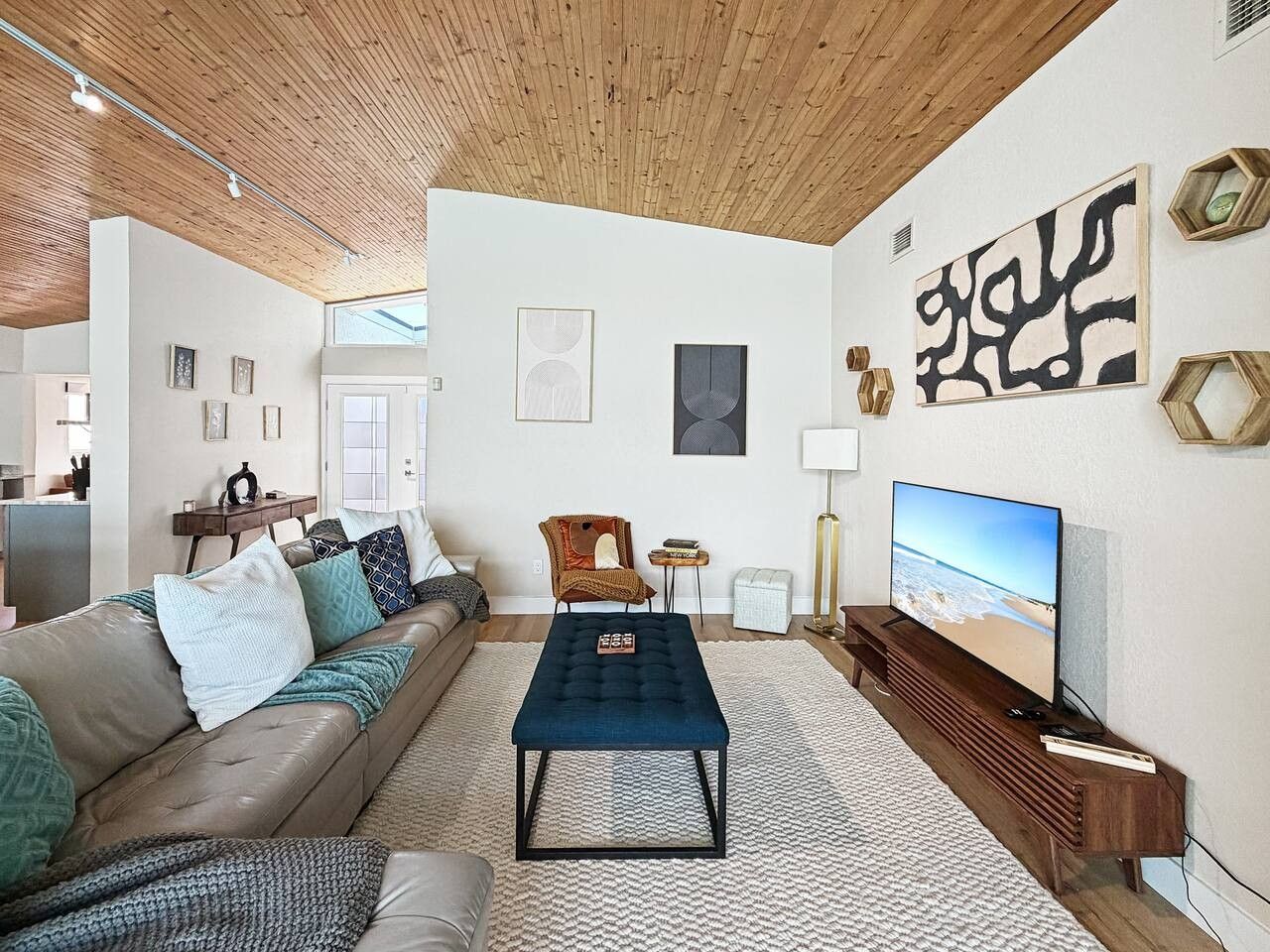 Un salon moderne avec un canapé, un pouf et un téléviseur à écran plat.