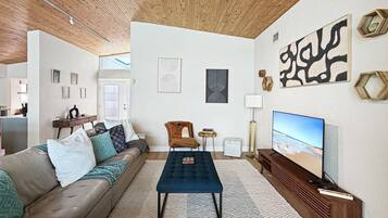 Un salon moderne avec un canapé, un pouf et un téléviseur à écran plat.