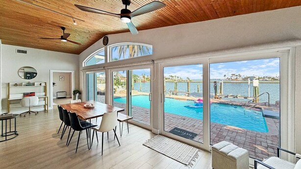 Amplia habitación con techo de madera, comedor y grandes ventanales con vistas a una piscina.