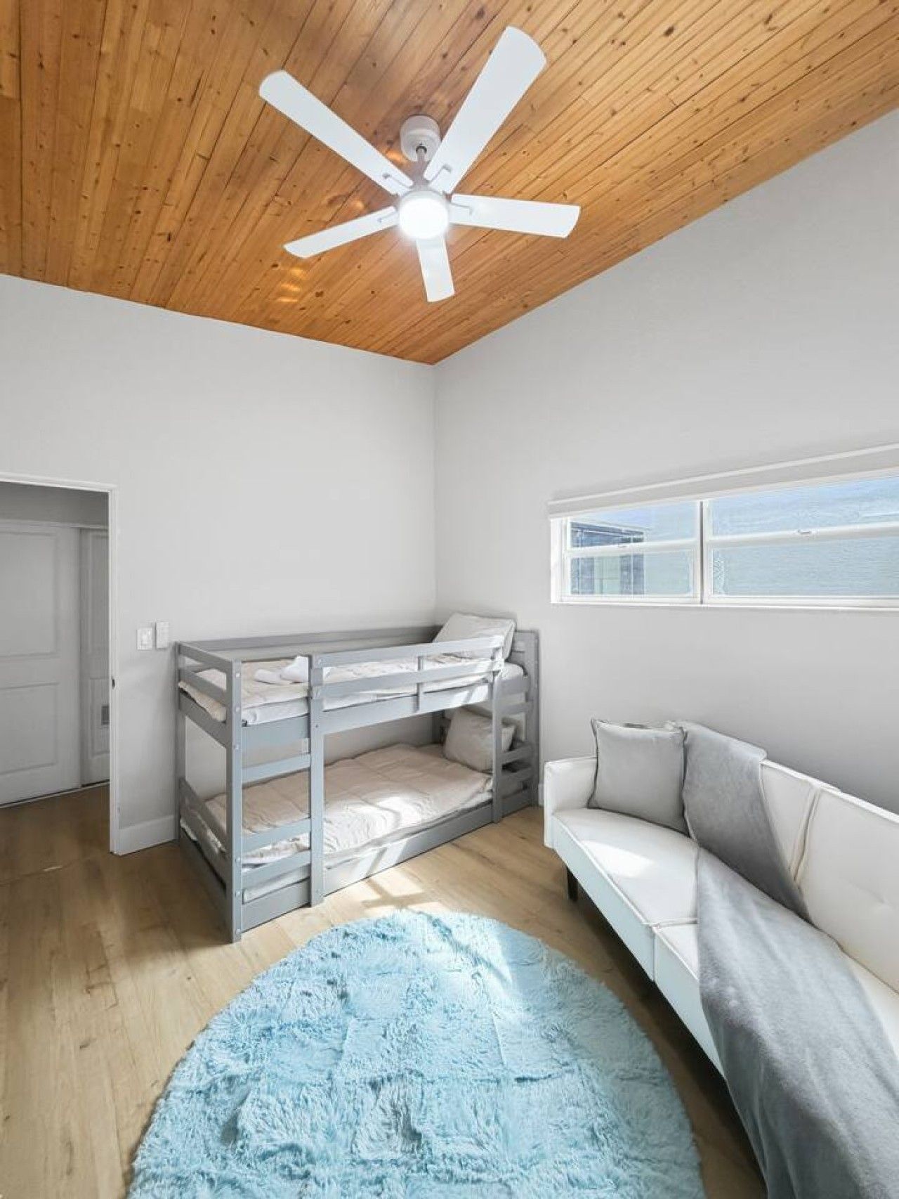 A room with a bunk bed, a sofa, a ceiling fan, and a window with a view.