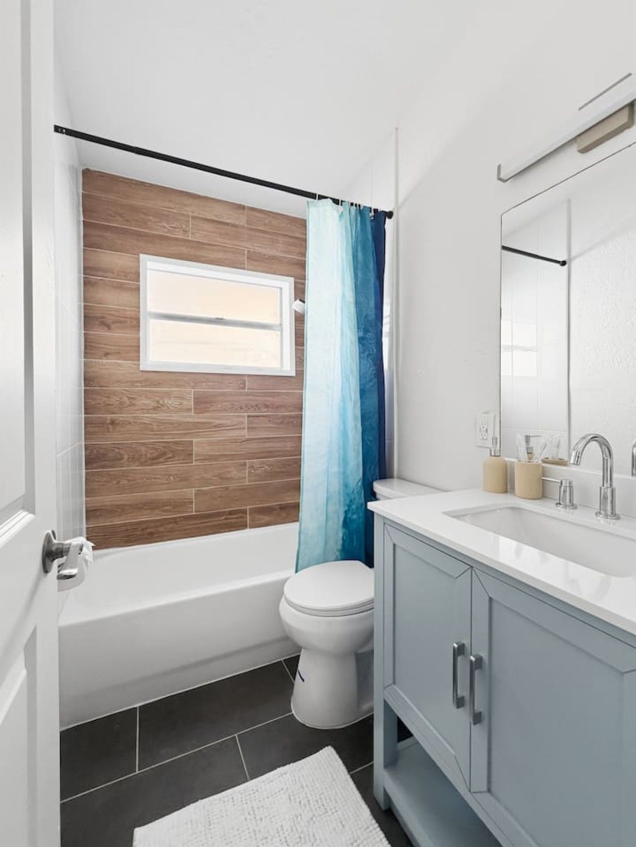 A modern bathroom with a wooden wall, a white toilet, a bathtub, and a vanity with a mirror.
