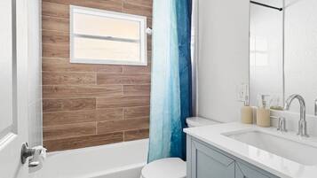 A modern bathroom with a wooden wall, a white toilet, a bathtub, and a vanity with a mirror.