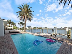 A swimming pool with a clear view of the water, a palm tree, and a dock extending into the water. - Coastal Haus|Luxe Waterfront | Dock | Sleeps 10 (Redington Beach)