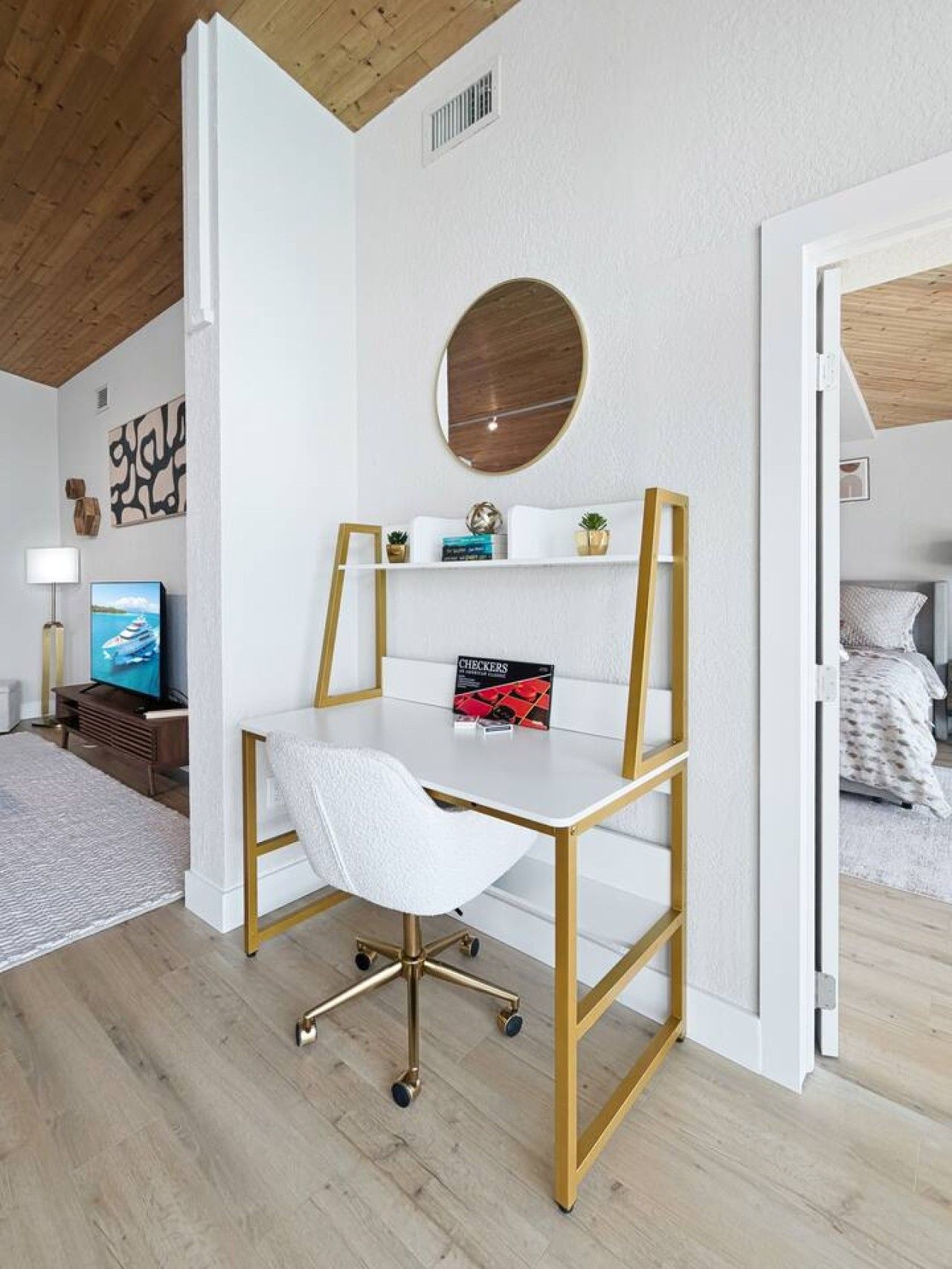 A modern bedroom with a white desk, a round mirror, and a bed with white bedding.