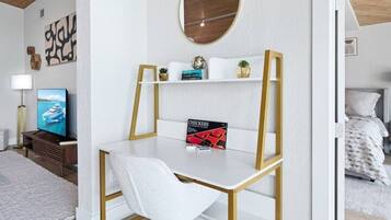 A modern bedroom with a white desk, a round mirror, and a bed with white bedding.