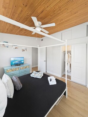Un dormitorio con una cama, ventilador de techo, televisor, cómoda y armario.