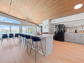 A modern kitchen with a large island, bar stools, and a view of the water. - Coastal Haus|Luxe Waterfront | Dock | Sleeps 10 (Redington Beach)