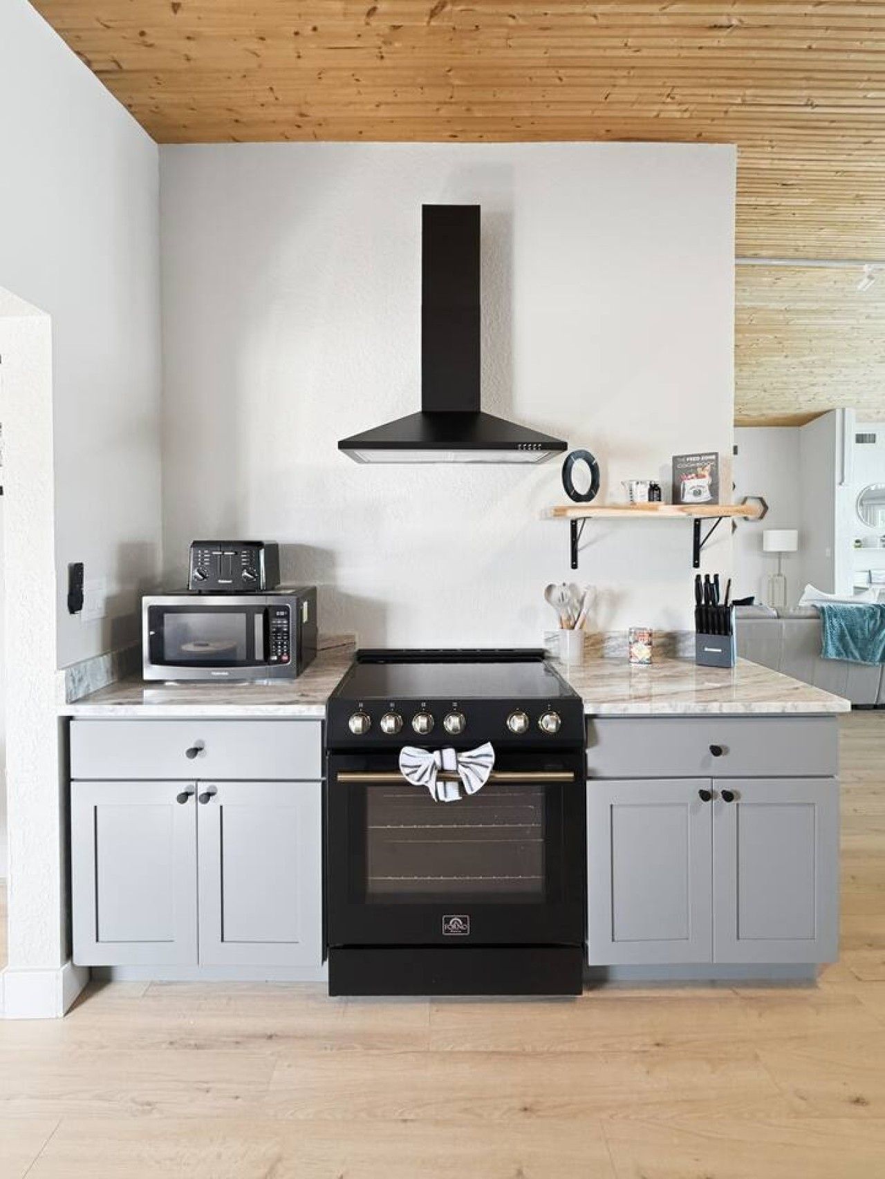 A kitchen with a microwave, stove, and oven, with a wooden ceiling and light-colored cabinets.