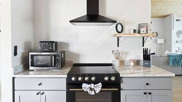 A kitchen with a microwave, stove, and oven, with a wooden ceiling and light-colored cabinets.