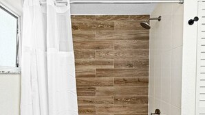Un baño con una bañera blanca, azulejos de madera y cortina de ducha blanca.