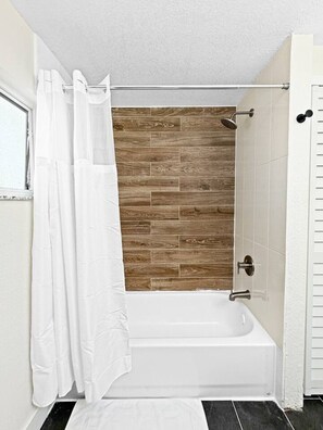 A bathroom with a white bathtub, wooden wall tiles, and a white shower curtain. - Coastal Haus|Luxe Waterfront | Dock | Sleeps 10 (Redington Beach)