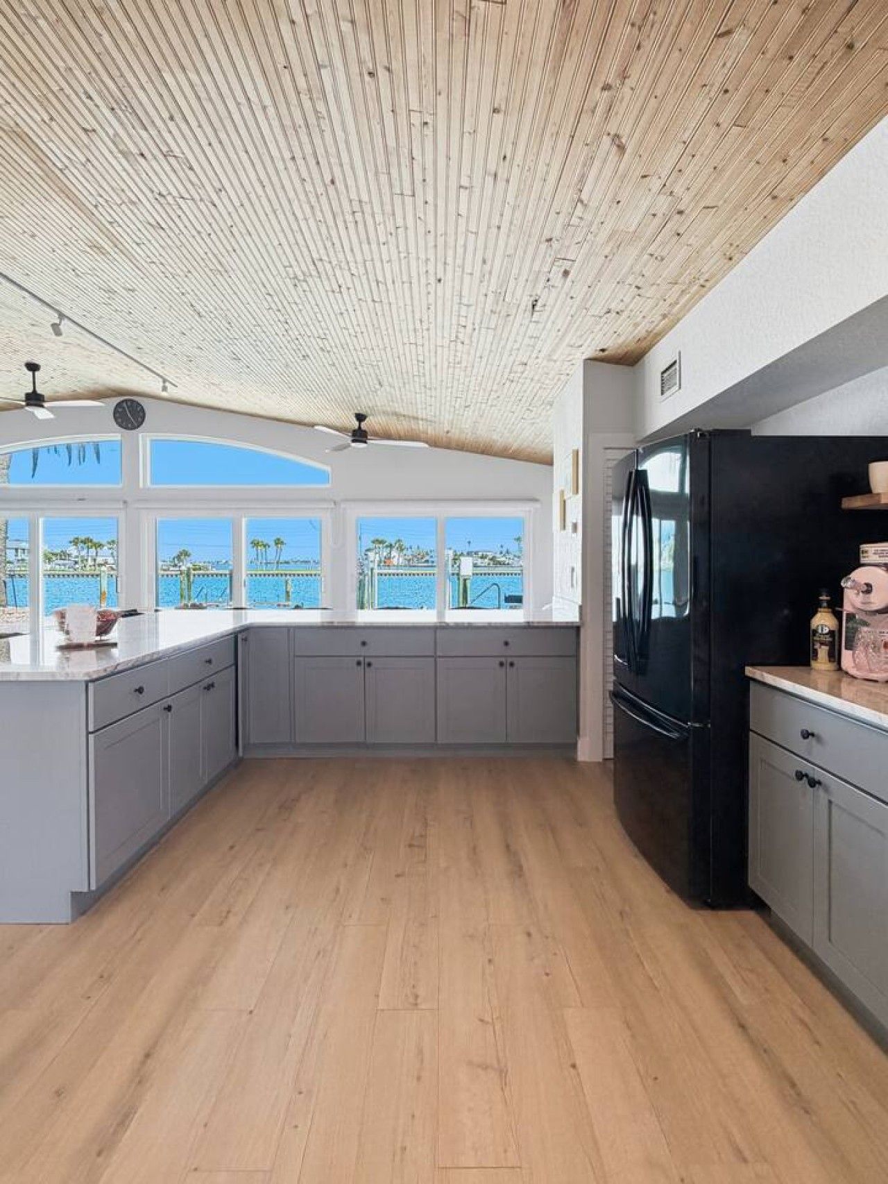 Een moderne keuken met een houten plafond, grijze kastjes en een zwarte koelkast.