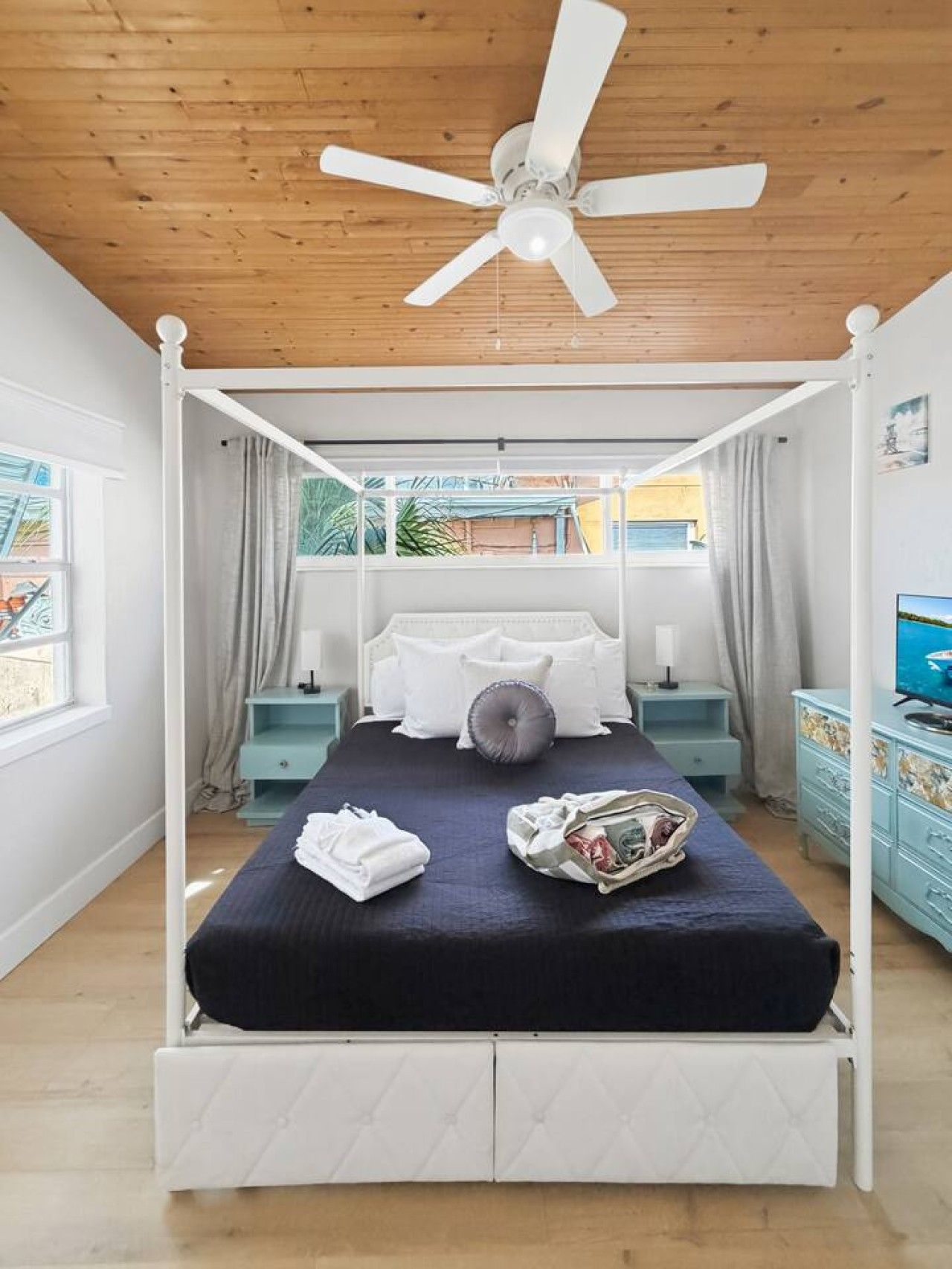 A four-poster bed with a ceiling fan, a television, and a view of the outdoors.