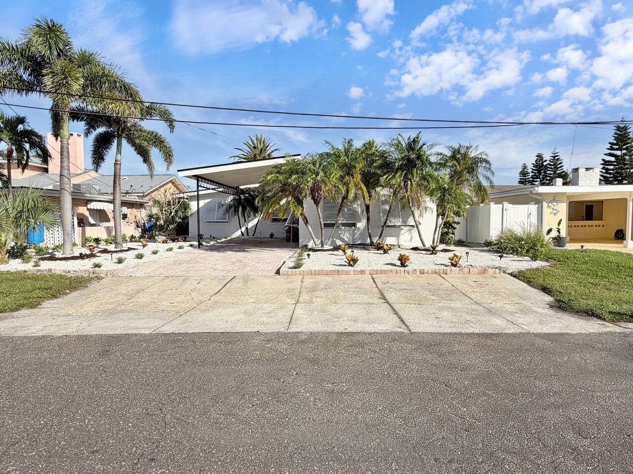 A residential area with a paved driveway leading to a house with a covered patio area.