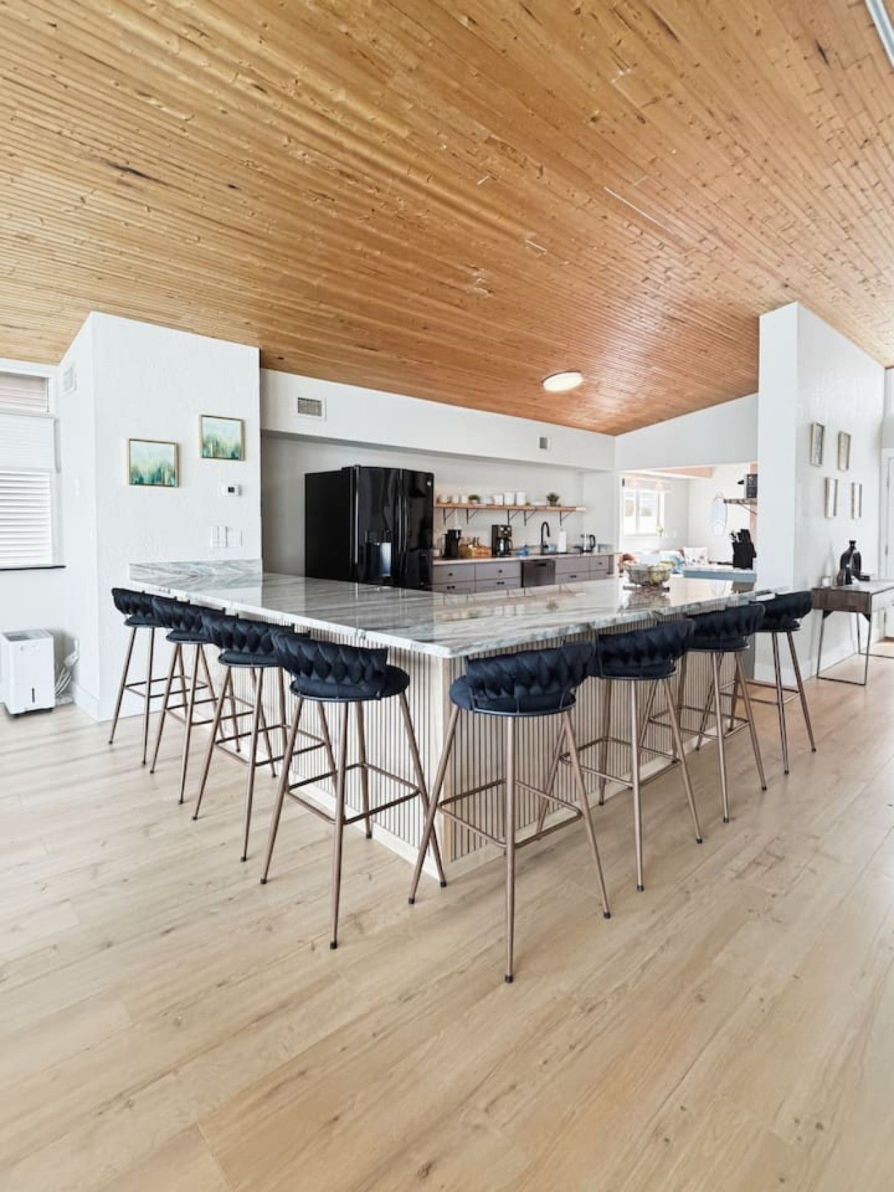 Une cuisine moderne avec un îlot central, des tabourets de bar et un plafond en bois.