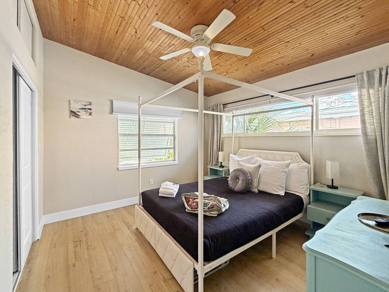 A four-poster bed with a ceiling fan, a bedside table, a nightstand, and a window with curtains.
