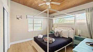 A four-poster bed with a ceiling fan, a bedside table, a nightstand, and a window with curtains.