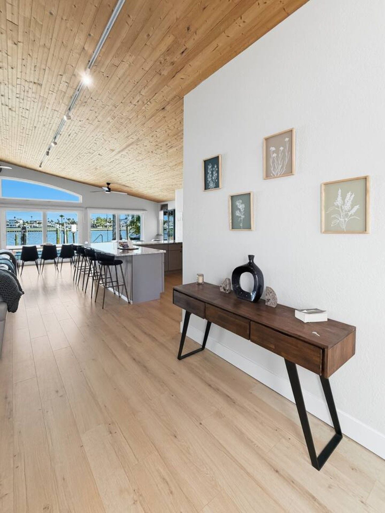 A modern interior with a wooden ceiling, a dining area with chairs, a kitchen, and framed artwork on the wall.