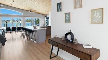 A modern interior with a wooden ceiling, a dining area with chairs, a kitchen, and framed artwork on the wall.