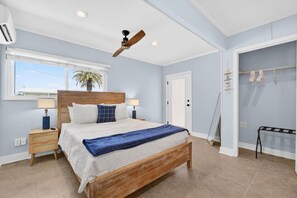 A bedroom with a wooden bed, two bedside tables, a ceiling fan, a window with blinds, and a door leading to a bathroom. - Sea Haus - Luxury Waterfront Pool Retreat - Beach (Redington Beach)