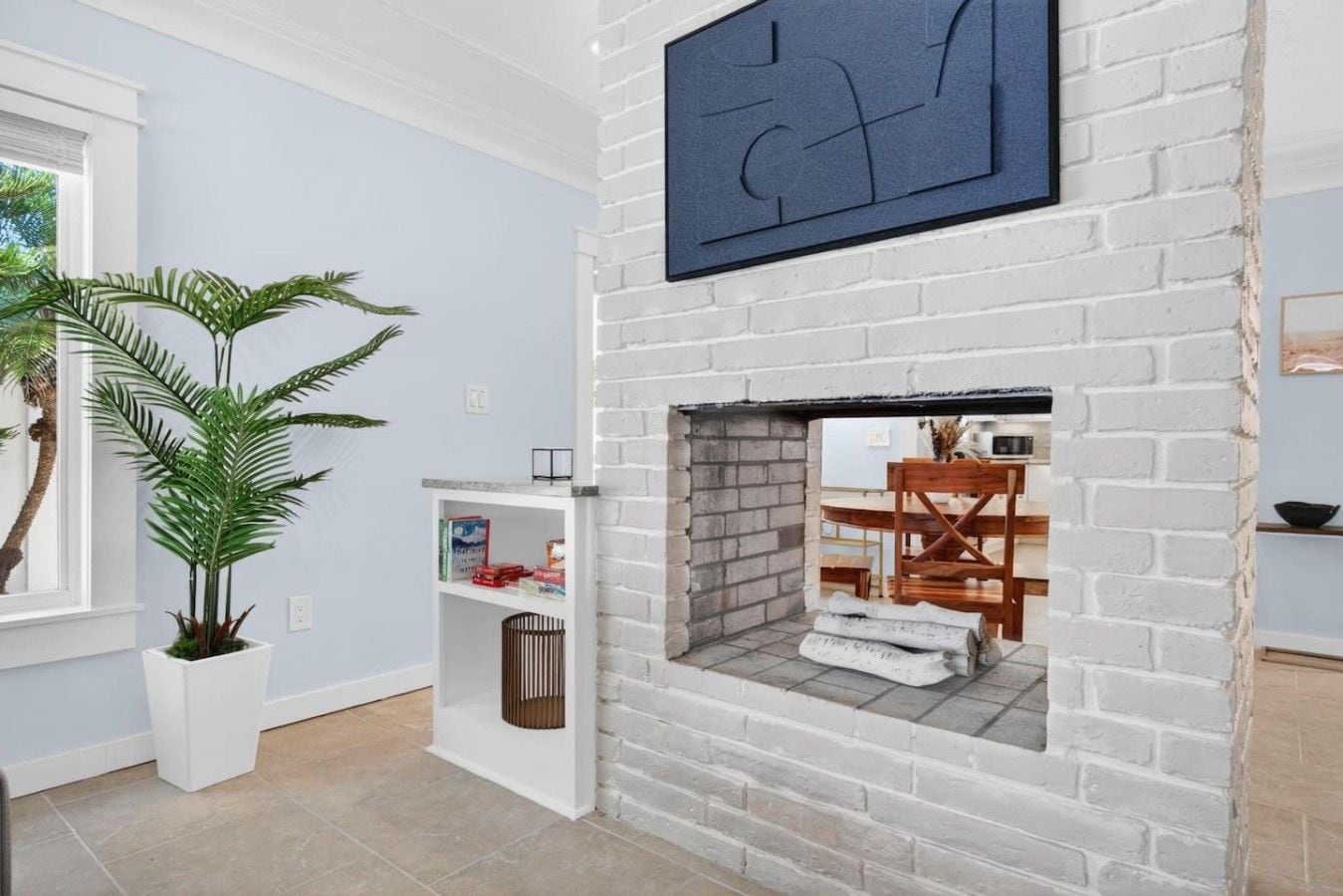 A room with a white brick fireplace, a potted plant, and a bookshelf.