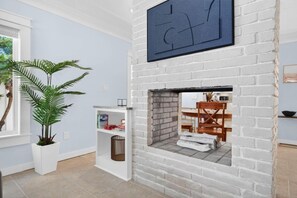 Une pièce avec une cheminée en briques blanches, une plante en pot et une bibliothèque.