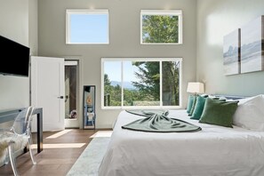 Un dormitorio con una cama grande, televisión y vistas a árboles y montañas.