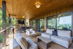 Eine Holzterrasse mit Gartenmöbeln, einem Grill und großen Fenstern mit Blick.