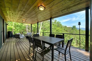 En overdækket terrasse med et bord og stole med udsigt over et skovområde.