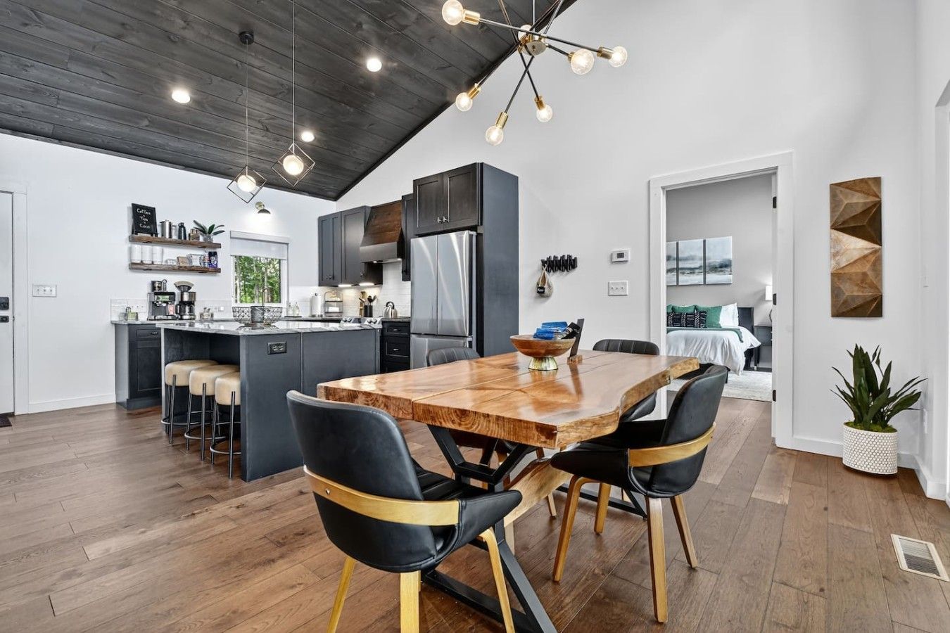 A modern kitchen with dark cabinetry, a central island, and a dining area with a wooden table and black chairs.