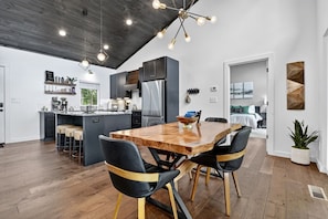 Una cocina moderna con armarios oscuros, una isla central y una zona de comedor con mesa de madera y sillas negras.
