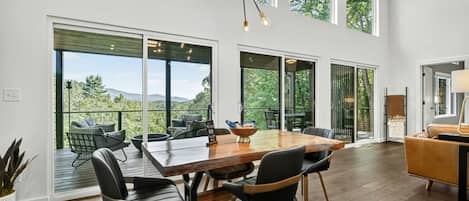A spacious dining area with a large wooden table, black chairs, and a view of the outdoors through large windows.